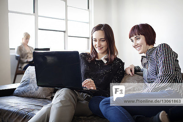 Happy businesswomen working on laptop while sitting on sofa in office