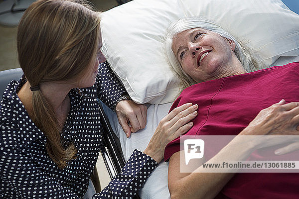 Smiling patient lying on bed while looking at daughter in hospital