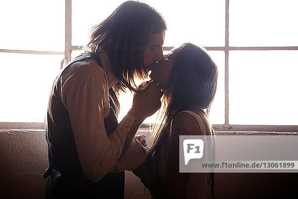 Seitenansicht eines Paares  das sich zu Hause am Fenster küsst
