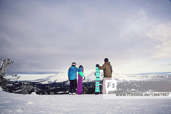 Freunde halten Snowboards in der Hand  während sie auf einem schneebedeckten Feld stehen