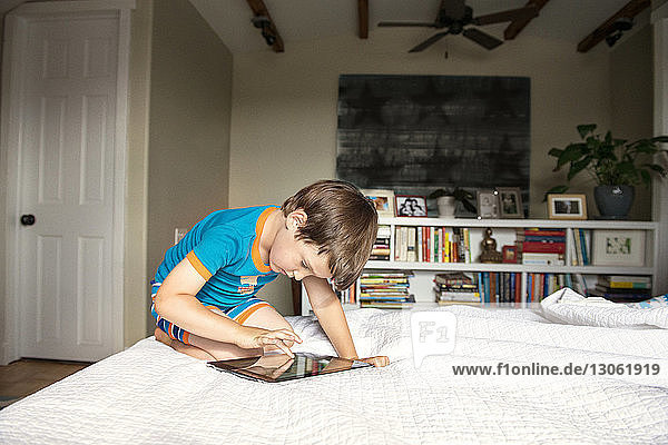Junge berührt Tablet-Computer  während er zu Hause auf dem Bett liegt