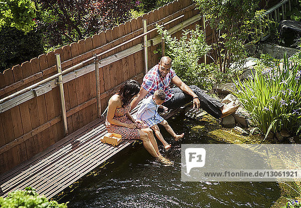 Hochwinkelaufnahme einer Familie  die auf einem Fußweg über einem Teich im Hinterhof sitzt