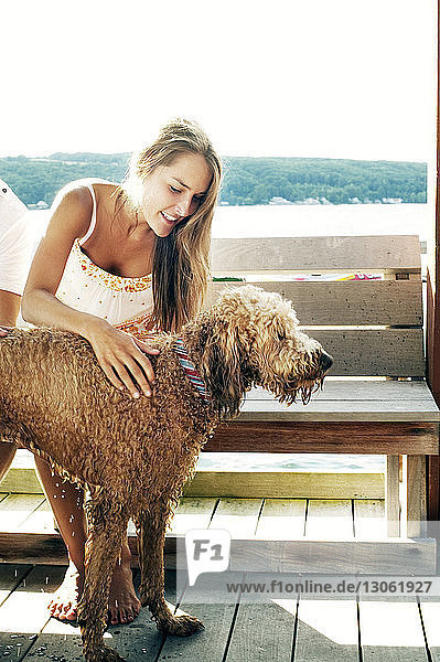 Glückliche junge Frau streichelt nassen Hund  während sie auf Bank sitzt