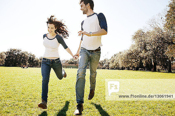 Paar rennt bei sonnigem Wetter auf einem Grasfeld im Park