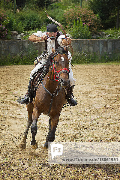 Man aiming with bow and arrow while riding horse