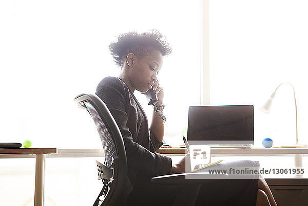 Seitenansicht einer Geschäftsfrau  die während eines Telefongesprächs im Büro sitzt