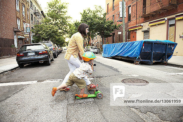 Mutter rennt mit ihrem Sohn auf einem Roller auf der Straße in der Stadt