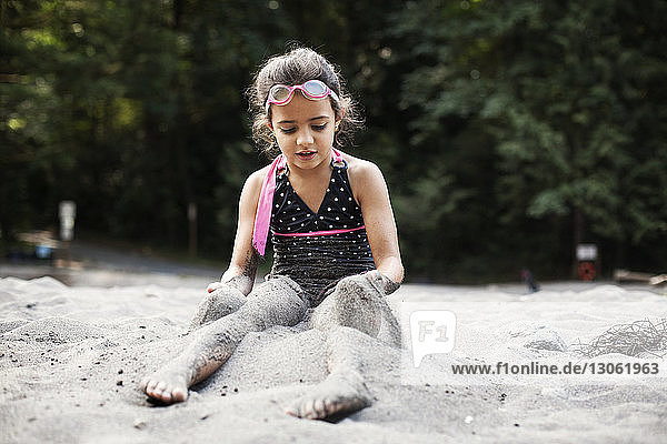 Girl putting sand on legs while sitting on shore at beach