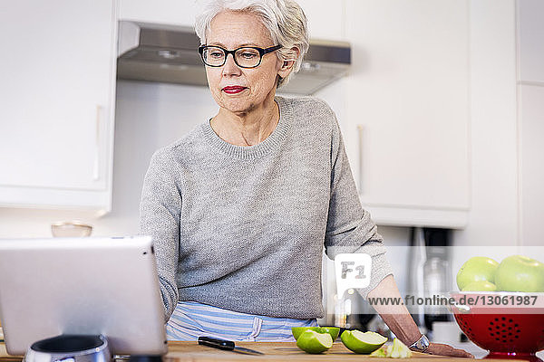 Ältere Frau betrachtet Rezept auf digitalem Tablett  während sie in der Küche steht