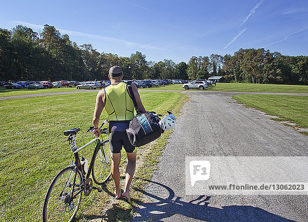 Rear view of man walking with bicycle on field