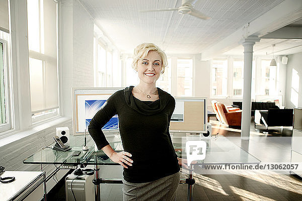 Portrait of smiling businesswoman standing by table in office