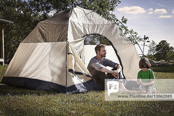 Father with son sitting by tent in lawn