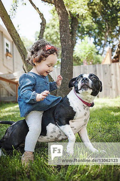 Glückliches kleines Mädchen sitzt auf Hund im Garten