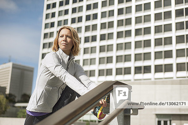 Frau schaut weg  während sie sich am Geländer gegen Gebäude in der Stadt streckt