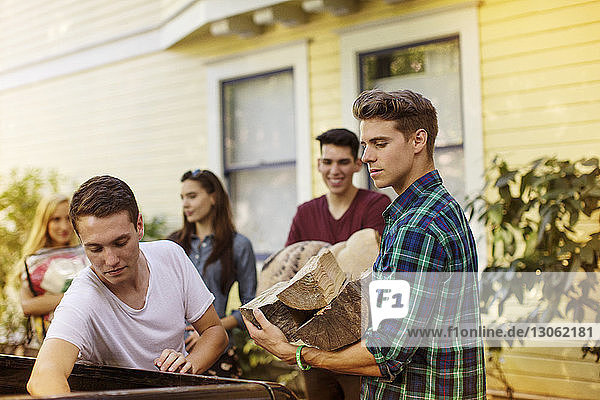 Mann hält Brennholz  während er vor dem Haus bei Freunden steht