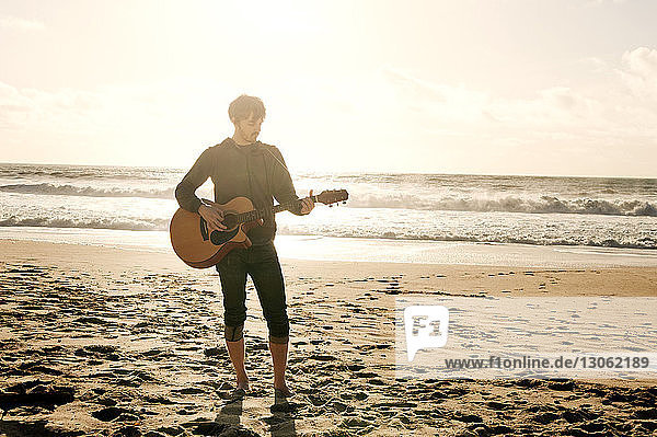 Mann spielt Gitarre  während er am Strand steht