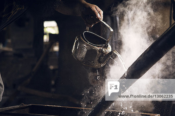 Geschnittene Hand eines Schmiedes gießt Wasser auf einen heißen Stab in der Werkstatt