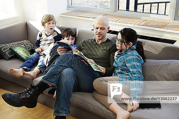 Family reading comic book while sitting on sofa at home