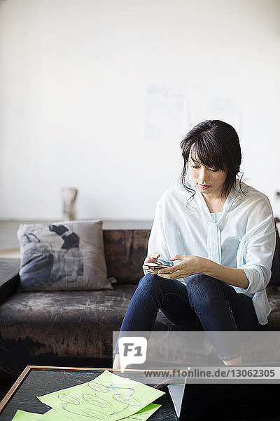 Geschäftsfrau schreibt Textnachrichten  während sie im Kreativbüro auf der Couch sitzt