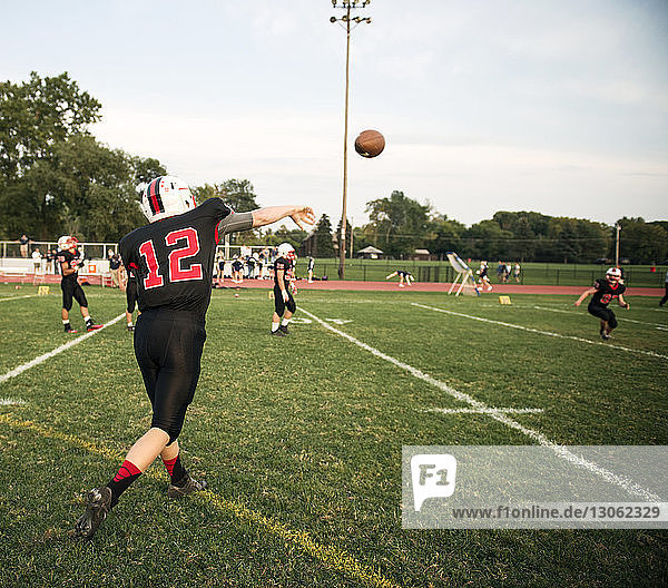 Rear view of teenage American football player throwing ball at field