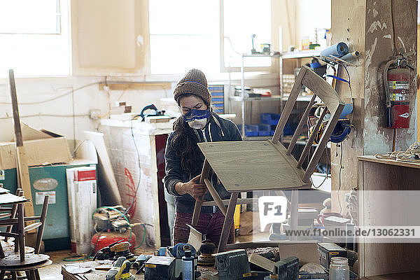 Female carpenter examining wooden chair in workshop