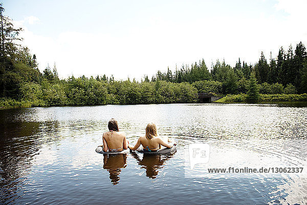 Rear view of female friends swimming on lake against sky