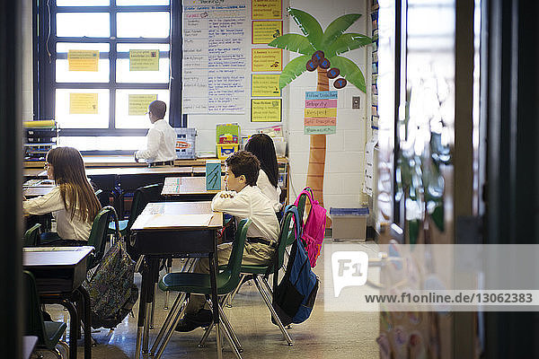 Children sitting at desks in classroom seen through doorway