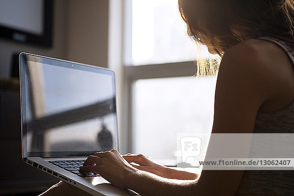 Frau benutzt Laptop  während sie zu Hause am Fenster sitzt