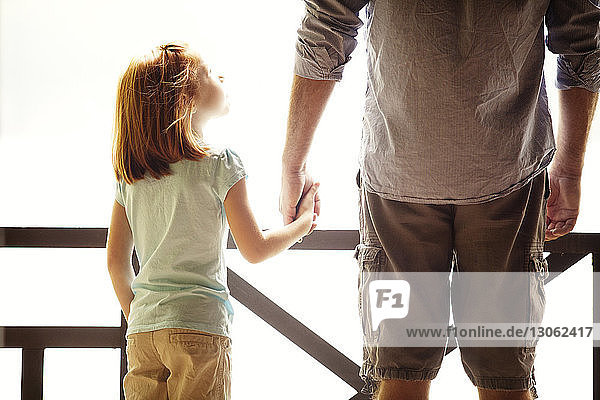 Rückansicht der Tochter  die die Hand des Vaters hält  während sie mit ihm auf dem Balkon steht