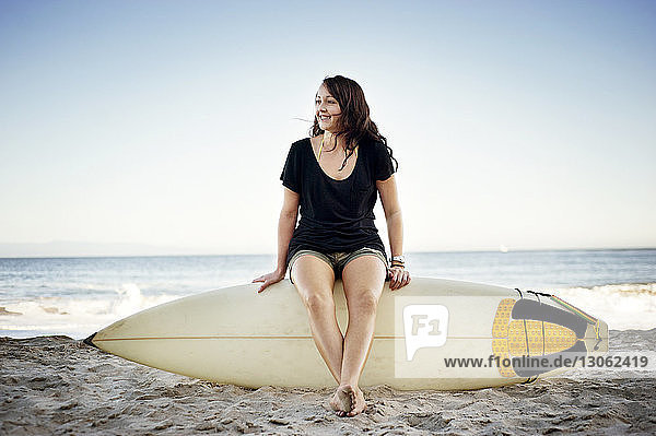 Frau schaut weg  während sie am Strand auf dem Surfbrett sitzt