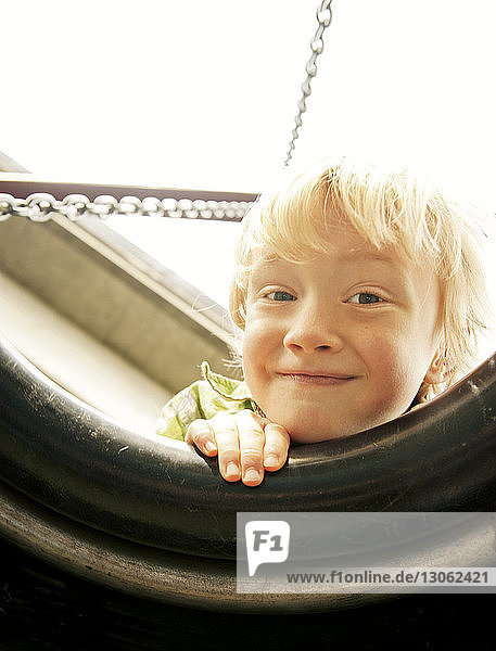 Porträt eines glücklichen Jungen  der durch die Reifenschaukel schaut