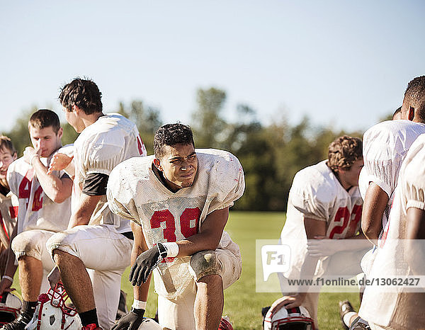 Football players kneeling at playing field on sunny day