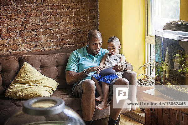 Father showing tablet computer to son while sitting on sofa at home