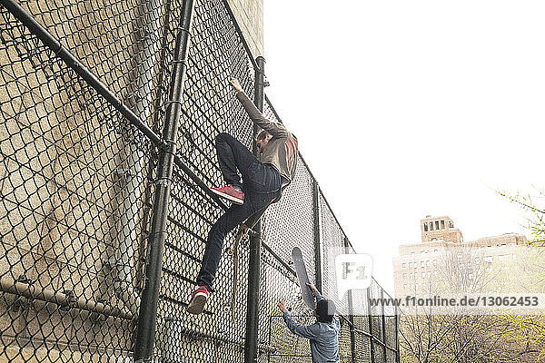 Friends climbing on chainlink fence at skateboard park