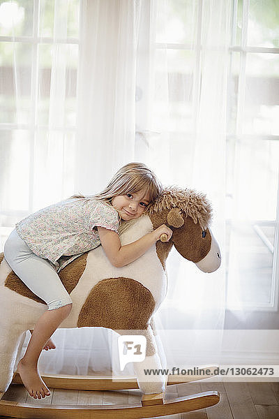 Portrait of smiling girl sitting on rocking horse against curtains at home