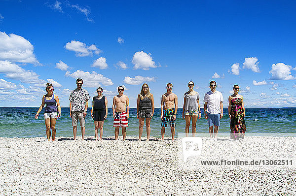 Friends standing on beach against sky on sunny day