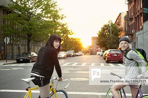 Portrait of friends with bicycles on city street during sunset