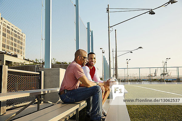 Happy father and son sitting on bleachers at soccer field