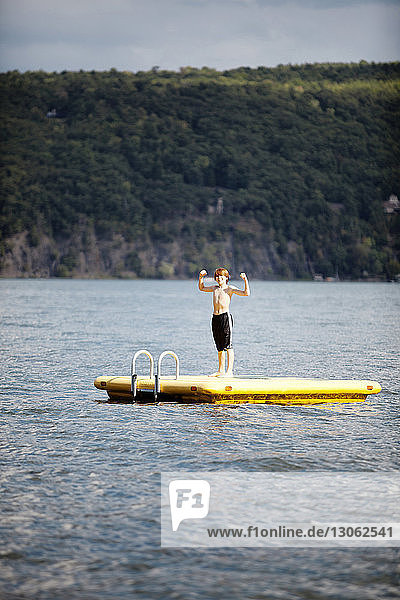 Junge beugt Muskeln  während er auf schwimmender Plattform im See steht