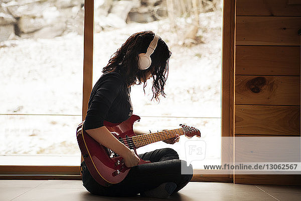 Seitenansicht eines jugendlichen Mädchens  das zu Hause auf dem Boden sitzend Gitarre spielt