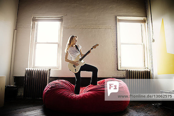 Junge Frau spielt zu Hause E-Gitarre auf Bean Bag
