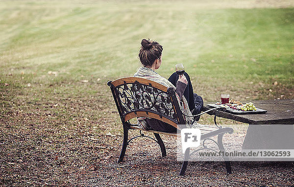 Frau hält Getränk in der Hand  während sie sich auf der Bank entspannt