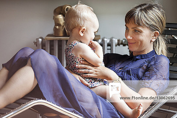 Mutter spielt mit Baby  während sie zu Hause auf einem Liegestuhl sitzt