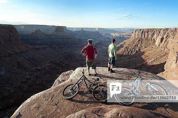 Rear view of mountain bikers standing on cliff