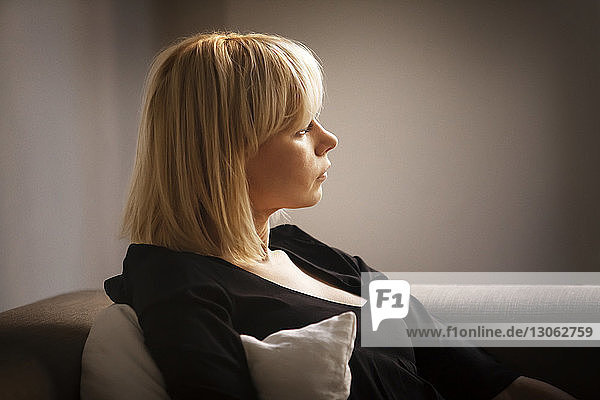 Frau schaut weg  während sie zu Hause auf dem Sofa sitzt