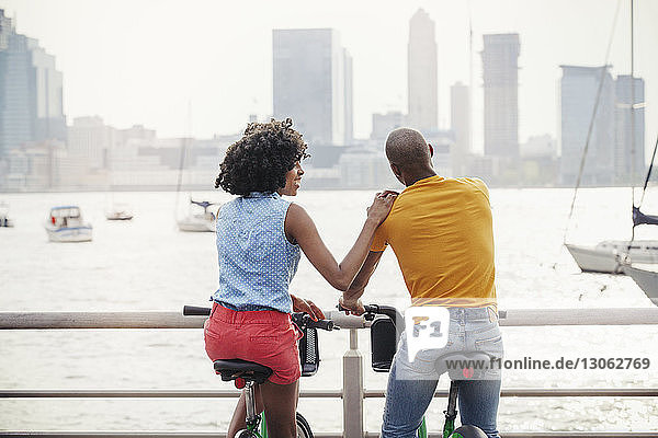 Rear view of couple sitting on bicycles against river in city