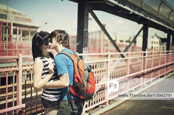 Mann küsst Freundin  während er an einem sonnigen Tag an einer Brücke steht