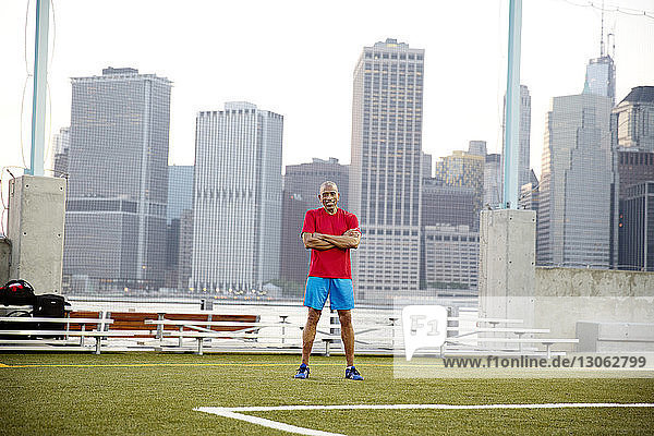 Portrait of confident senior man standing on soccer field in city