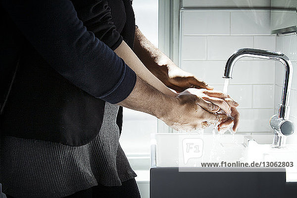 Mittelteil eines Liebespaares beim Händewaschen im Badezimmer