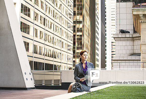 Geschäftsfrau hält Tablet-Computer in der Hand  während sie auf einer Stützmauer sitzt